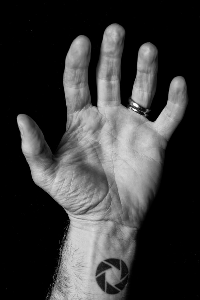 Black and white shot of a man hand with aperture tattoo on the wrist and rings on finger