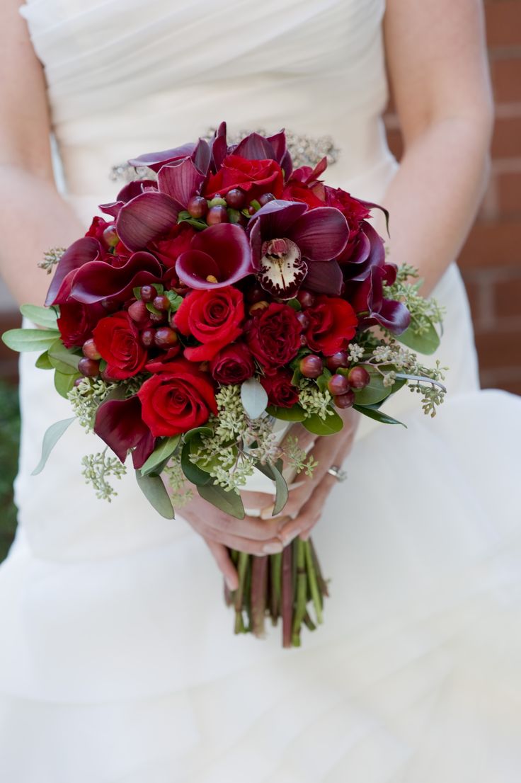 Burgundy cymbidium orchid blooms, red roses and calla lilies arranged beautifully in this bridal bouquet
