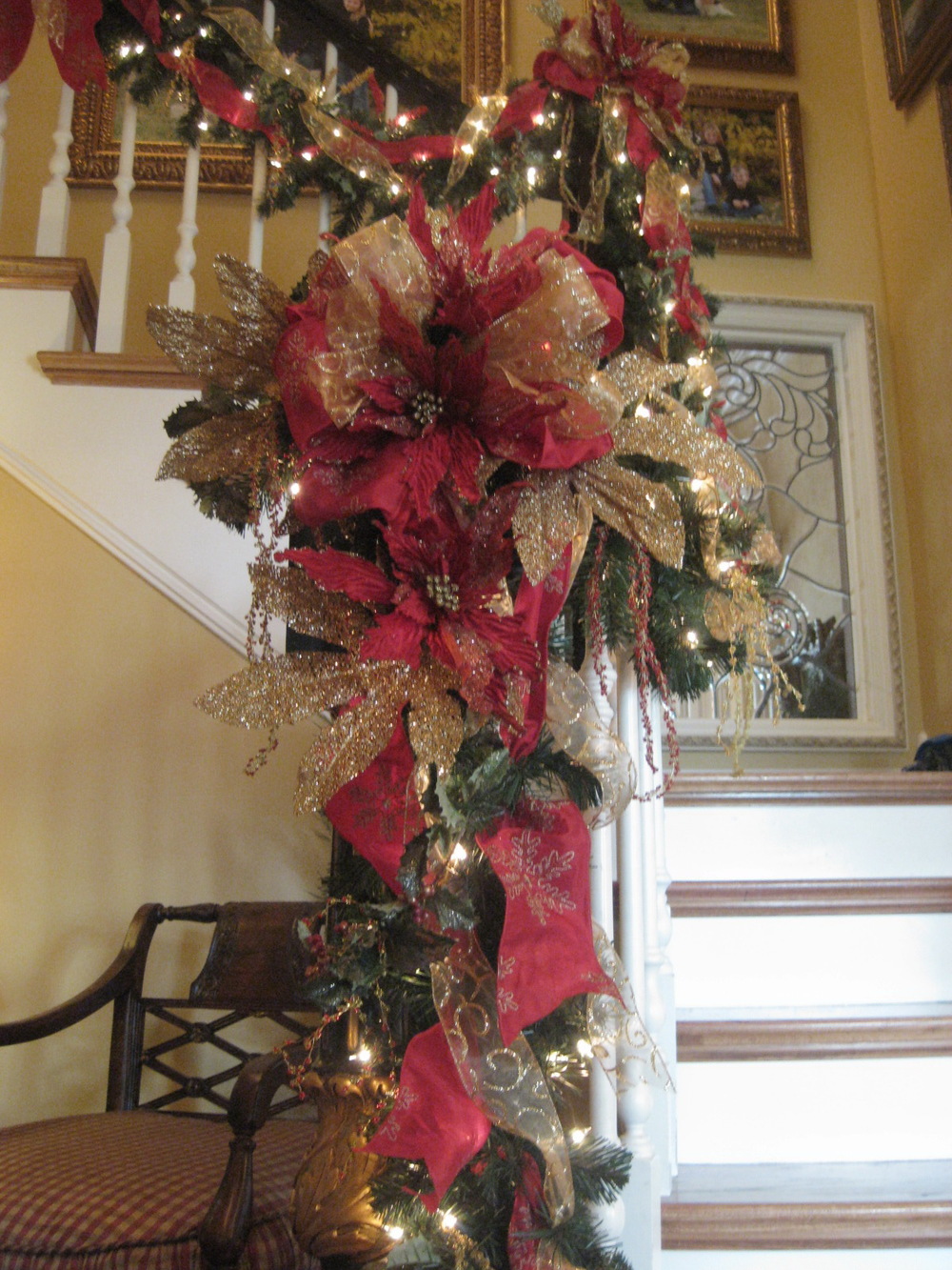 Gorgeous Christmas staircase with beautiful ribbon, poinsettias, glittered leaves, and hanging beaded berries.